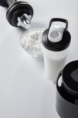 selective focus of sports bottle with protein shake near jar and dumbbell on white  clipart