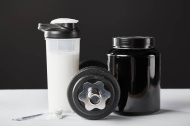 Kaşık dambıl yanında ve siyah protein içeceği ile spor şişesi. 