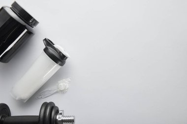 Dambıl, kavanoz ve spor şişesinin yanında beyaz kaşık ve protein bulunan üst görünümü 