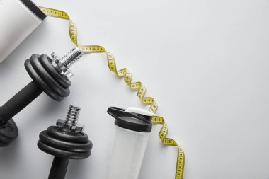 top view of sports bottle and measuring tape near heavy dumbbells on white  clipart