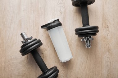 top view of sports bottle near heavy dumbbells on wooden surface  clipart