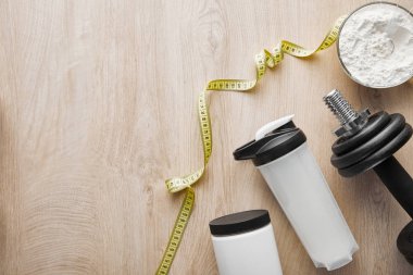 Spor şişesinin yanındaki ağır dambılların ve tahta yüzeydeki şeritlerin üst görüntüsü 