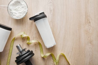 Spor şişesinin yanındaki dambılın üst görüntüsü ve ahşap yüzey üzerindeki şerit. 