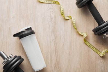 top view of dumbbells near sports bottle with protein shake near measuring tape on wooden surface  clipart