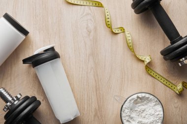Spor şişesinin yanındaki dambılların ve tahta yüzeydeki şeritlerin üst görüntüsü 