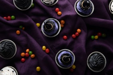 top view of delicious Halloween cupcakes with bonbons on purple cloth clipart