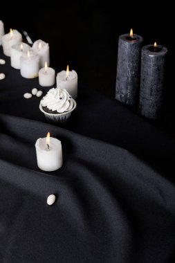 Siyah arka planda yanan mumların yanında beyaz kremalı lezzetli Cadılar Bayramı keki.