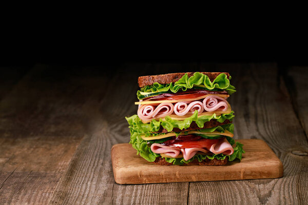 Свежий сэндвич с салатом, ветчиной, сыром, беконом и помидорами на деревянной доске
