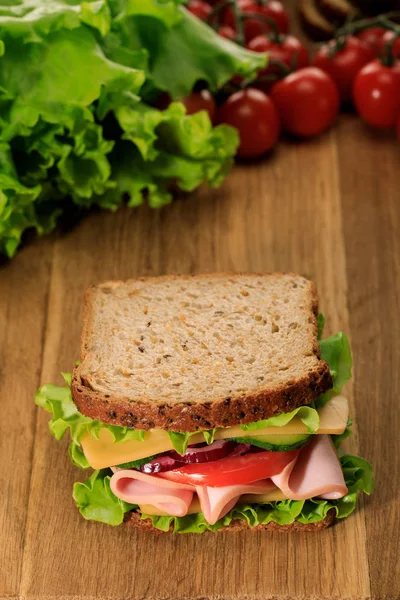 在生菜和樱桃西红柿附近的木制切菜板上选择性地添加新鲜三明治 — 图库照片