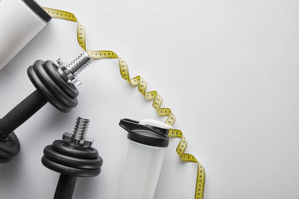 top view of sports bottle and measuring tape near heavy dumbbells on white 