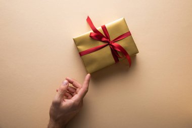 Kırpılmış insan manzarası bej arka planda kırmızı kurdeleli altın hediye kutusuna dokunuyor.