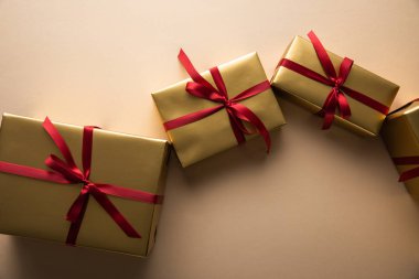 Kırmızı kurdeleli ve bej arkaplanlı altın hediye kutularının üst görünümü