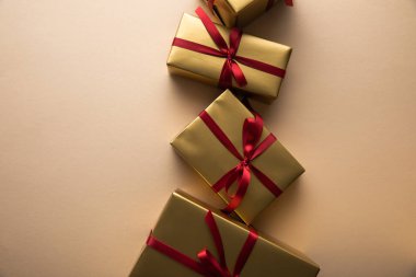 Kırmızı kurdeleli ve bej arkaplanlı altın hediye kutularının üst görünümü