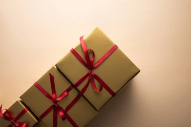 Kırmızı kurdeleli ve bej arkaplanlı altın hediye kutularının üst görünümü
