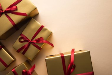 Kırmızı kurdeleli ve bej arkaplanlı altın hediye kutularının üst görünümü