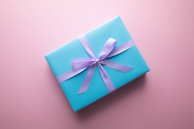 Pembe arka planda mor saten kurdeleli mavi hediye kutusunun üst görünümü