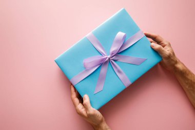 cropped view of man holding blue gift box with violet satin ribbon on pink background clipart