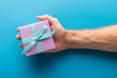 Mavi arka planda menekşe rengi hediye kutusu tutan adamın kırpılmış görüntüsü