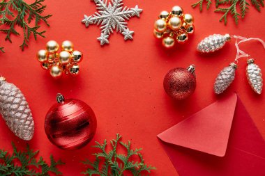 Kırmızı arka planda parlak Noel dekorasyonu, zarf ve thuja manzarası