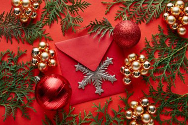 Parlak Noel dekorasyonunun üst görüntüsü, kırmızı arka planda kar tanesi ve thuja ile kaplı zarf