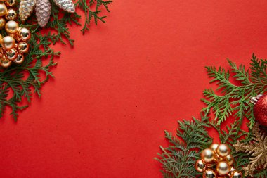 Kırmızı zemin üzerinde yeşil thuja dalları ve fotokopi alanı üzerine parlak Noel dekorasyonunun üst görünümü
