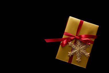 Kırmızı kurdeleli ve siyah kartaneli parlak altın bir Noel hediyesi.