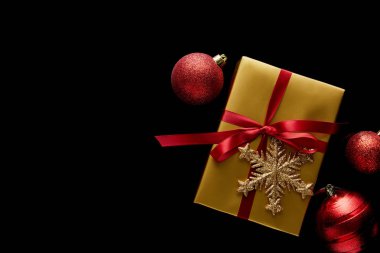 Kırmızı kurdeleli ve mücevherlerin yakınındaki kar taneli parlak altın noel hediyesinin en üst görüntüsü siyah üzerine izole edilmiş.