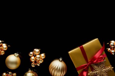 Kırmızı kurdeleli ve mücevherlerin yakınındaki kar taneli parlak altın noel hediyesinin en üst görüntüsü siyah üzerine izole edilmiş.