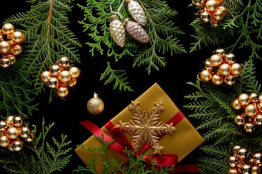 top view of shiny golden Christmas decoration, green thuja branches and gift box isolated on black clipart
