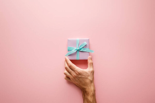 обрезанный вид человека с фиолетовой маленькой подарочной коробочкой с синей атласной лентой на розовом фоне
