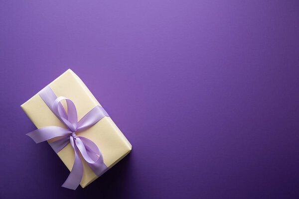 top view of gift box with violet ribbon on purple background with copy space