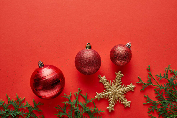 Верхний вид блестящих рождественских безделушек, еловых ветвей и золотистой снежинки на красном фоне
