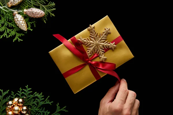 輝く黄金のクリスマスの装飾の近くの贈り物に弓を結ぶ男のクロップドビュー黒に隔離された緑のThujaの枝 — ストック写真