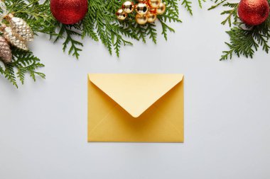 Parlak altın noel süslemesi ve beyaz renkli yeşil thuja dallarının yakınındaki zarf.