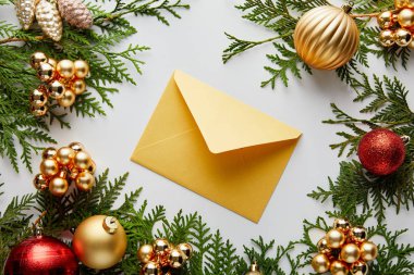 Yeşil thuja dalları üzerindeki parlak altın ve kırmızı Noel süslemesi ve beyaz üzerine izole edilmiş bir zarf.