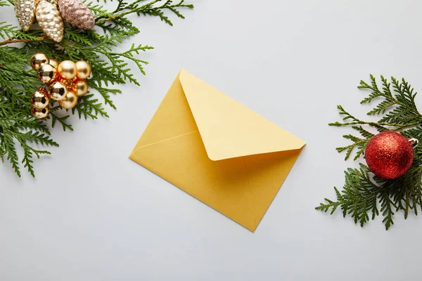 白に隔離された封筒の近くの緑のトゥヤの枝に輝く黄金と赤のクリスマスの装飾のトップビュー — ストック写真