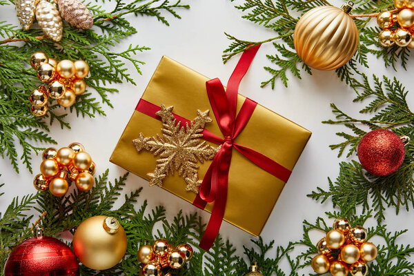 верхний вид на блестящие золотые и красные рождественские украшения на зеленые ветви туи, завернутый подарок со снежинкой изолированы на белом
