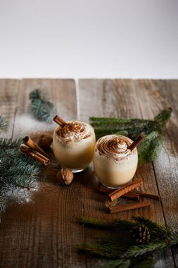çırpılmış krema ve tarçınlı eggnog kokteyli ladin dallarının yanında ve pudra şekeri gri masaya saçılmış.