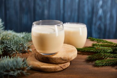 Lezzetli eggnog kokteyli yuvarlak ahşap tahtalar üzerinde ladin dallarının yanında mavi desenli arka planda. 
