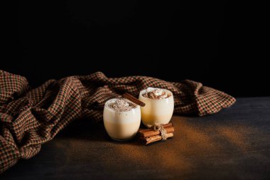 Lezzetli eggnog kokteyli, tarçın çubukları ve kareli kumaş. Siyah üzerine izole edilmiş tarçın tozu ile kaplı.