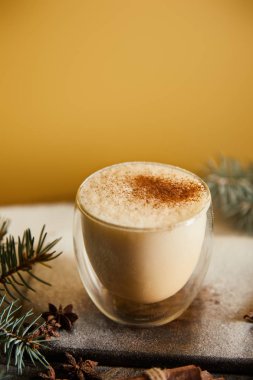 Spruce dallarının yanında tarçınlı geleneksel eggnog kokteyli ve turuncu arka planda dağınık şeker tozu.