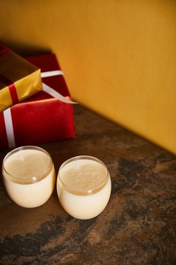 Lezzetli eggnog kokteyli ve hediye kutuları turuncu duvarın yanındaki koyu mermer masada.