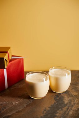 Lezzetli eggnog kokteyli ve portakallı koyu mermer masada hediye kutuları.
