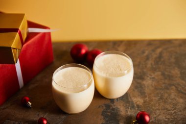 Lezzetli eggnog kokteyli, hediye kutuları ve portakallı koyu mermer masa üzerindeki Noel topları.