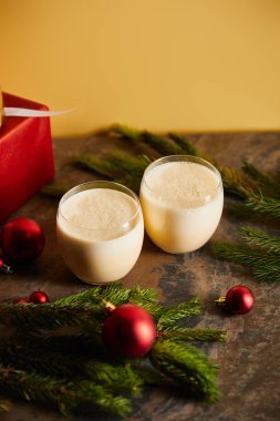Lezzetli eggnog kokteyli, hediye kutuları, ladin dalları ve portakallı koyu mermer masa üzerindeki Noel topları.