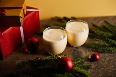 Geleneksel eggnog kokteyli, hediye kutuları, ladin dalları ve portakallı koyu mermer masa üzerindeki Noel topları.