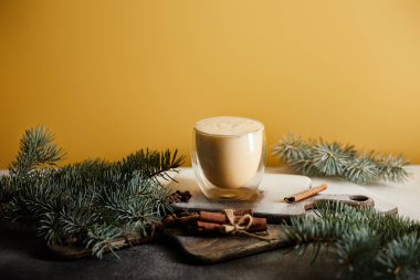 eggnog kokteyli şeker tozu, ladin dalları ve turuncu üzerine izole edilmiş tarçın çubuklarıyla kaplı masada.