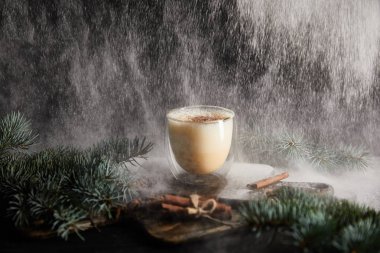 tasty eggnog cocktail on cutting board near spruce branches and cinnamon sticks on black background with powdered sugar falling like snow clipart