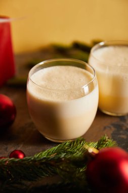 Geleneksel eggnog kokteyli, ladin dalları ve noel toplarını portakalda izole edilmiş koyu mermer masaya odakla.