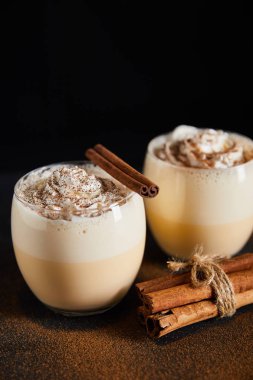 Nefis eggnog kokteyli. Krem şantili ve tarçın çubuklu. Masada tarçın tozu var.